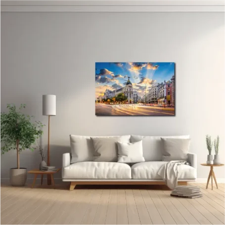 Sala luminosa con un sofá blanco, una lámpara y un cuadro de paisaje urbano en la pared.