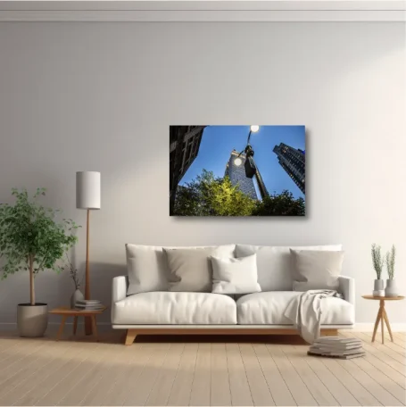 Sala luminosa con sofá, planta y cuadro de edificios en el fondo.