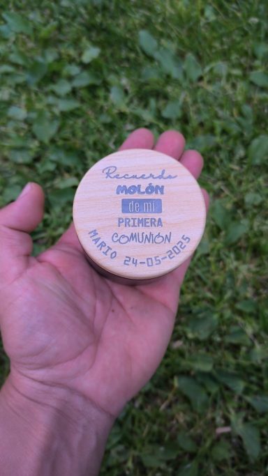 Una mano sostiene un objeto redondo con texto en azul sobre un fondo blanco.