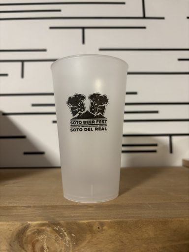 Vaso translúcido con un diseño negro de dos rostros en un fondo con rayas.