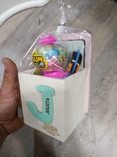 Caja decorativa con juguetes y útiles escolares, formada por un contenedor con la letra "J".