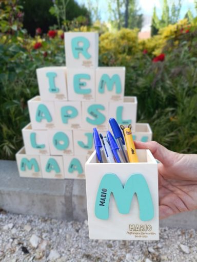 Cubos apilados con letras y un recipiente sosteniendo varios bolígrafos de colores.