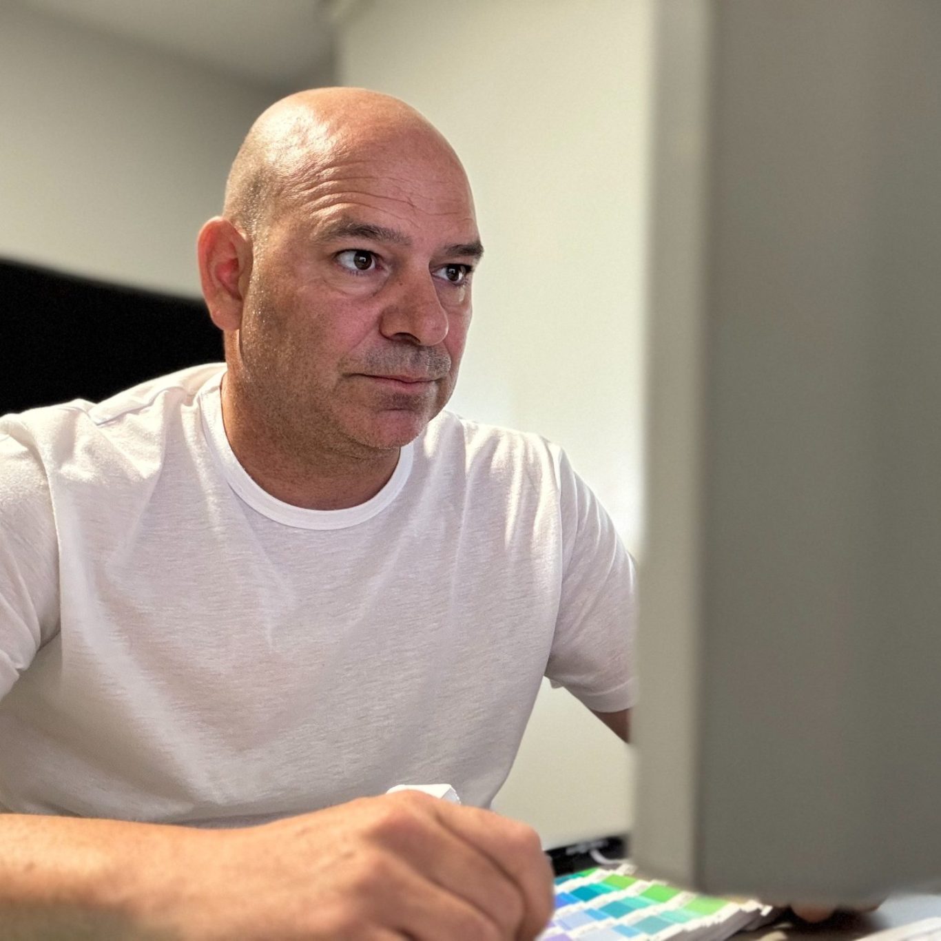 Hombre calvo concentrado en la computadora, vistiendo una camiseta blanca.